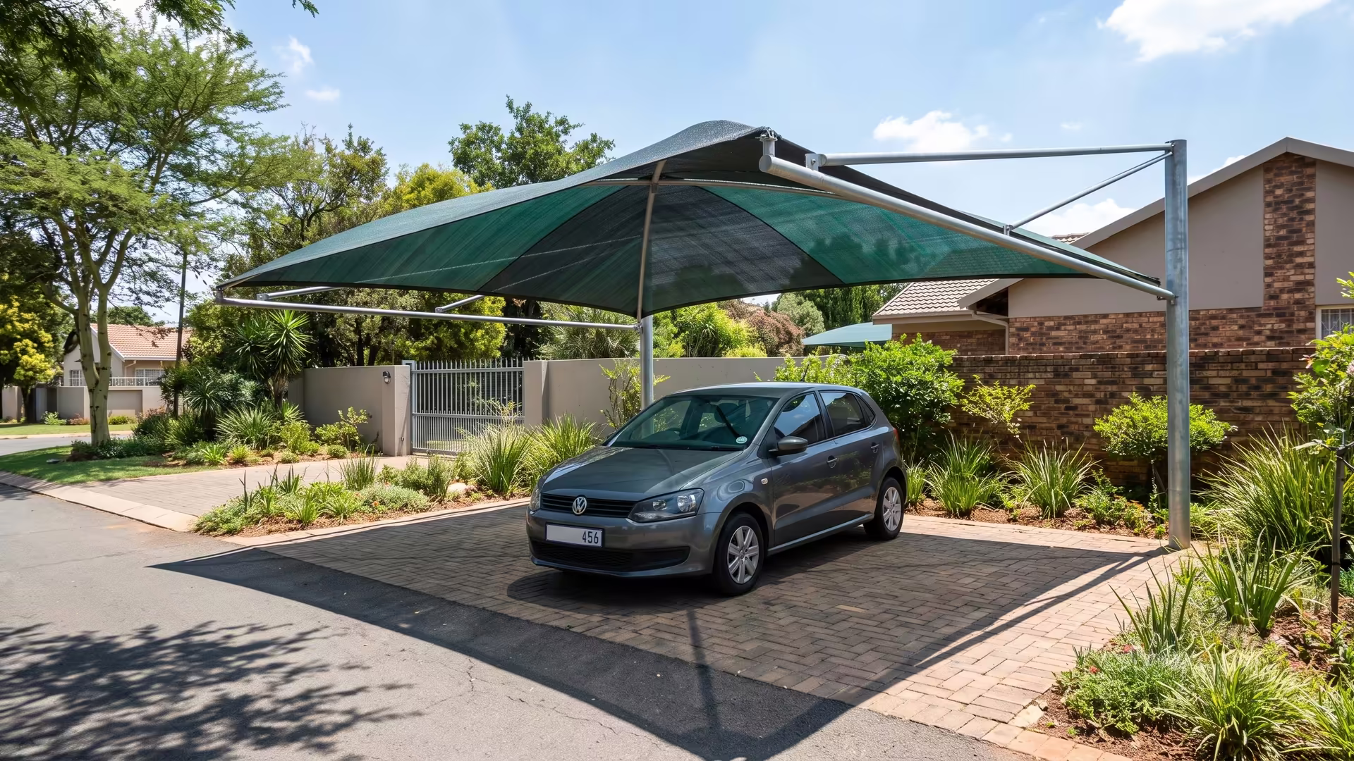 Shade-net shadeport with a green shade-cloth roof covering a car on a suburban driveway
